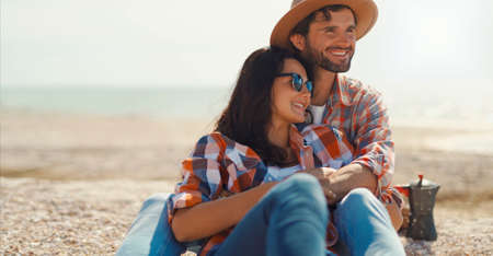 happy romantic couple sits on sea beach, talks, laughs and hugs. moments of loveの写真素材
