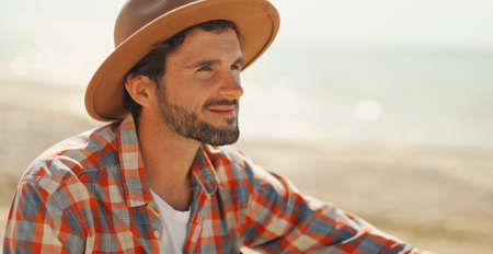 close up portrait of handsome stylish casual man traveler in hat sitting at sea coastline and enjoying peaceful natureの写真素材
