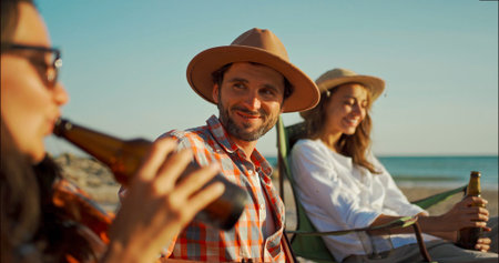 friends relaxing on beach with beer, sitting and relaxing on chairs on beach at seaside