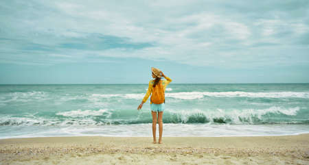 sea view with waves and cloudy sky, woman standing at beach in summer clothesの写真素材