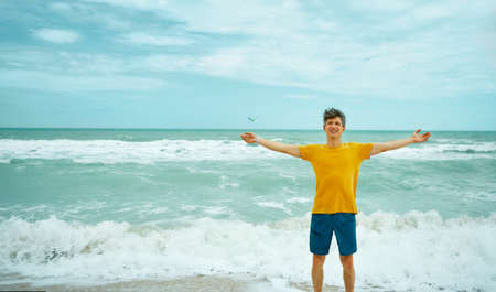portrait joyful happy man in yellow shirt with open arms enjoing holidays on beachの写真素材