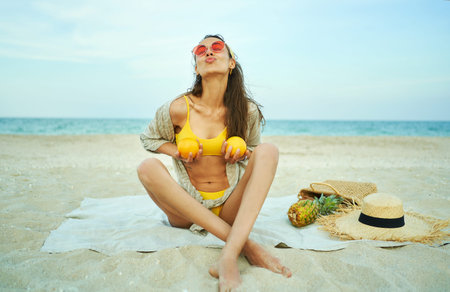 Funny playful young woman holding fruits over their breasts on the beachの写真素材