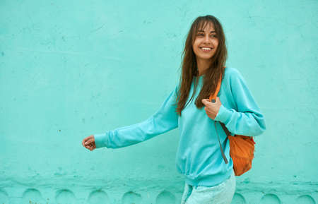 Satisfied young American woman with dark hair looking confident, walking along blue wall, total blue colorの写真素材