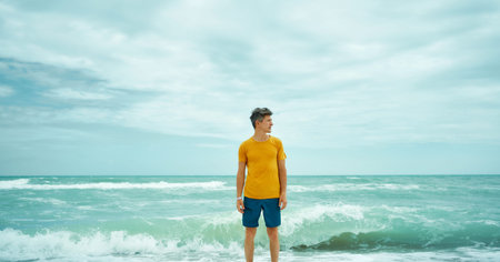 man in yellow shirt standing in sea water with waves, feeling calm and harmony