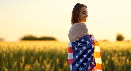 American woman covered with flag of america at sunset on wheat fieldの写真素材