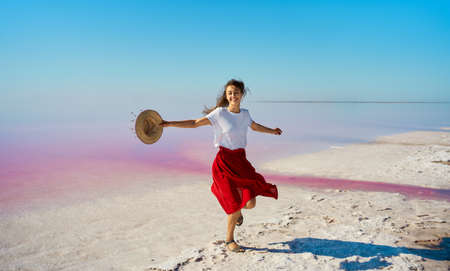 Happy smiling woman in red skirt dancing, dynamic moving at salt flats of pink lakeの写真素材