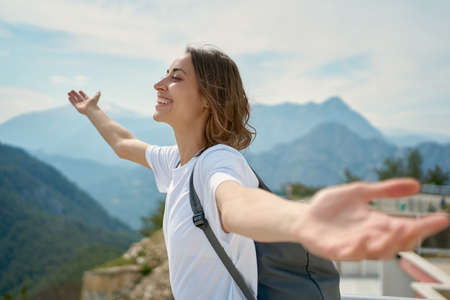side view traveler freedom woman with open arms laughing and enjoying mountains view, summer journey vacationの写真素材