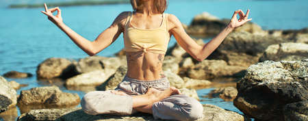 Close up female healthy slim body doing yoga in lotus pose with hand gesture mudra, morning yoga meditation practice outdoorsの写真素材