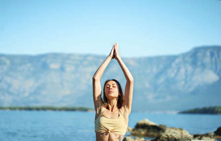 Portrait woman doing morning yoga session process meditation practice, sun salutation and breathing exercises with mountains landscapeの写真素材