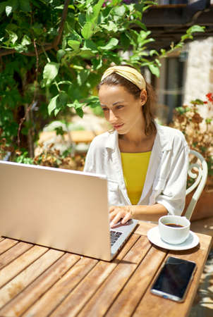 Concentrated young business woman using laptop computer, checking notification for laptop system, working in cafe during vacationの写真素材