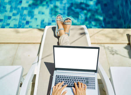 top view woman working on laptop computer with white blank screen, female hands typing keyboarding text, lying by the poolの写真素材