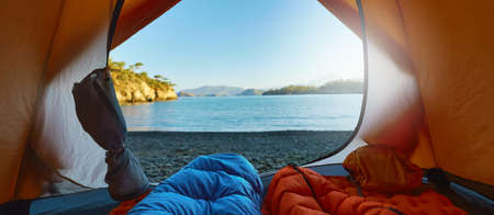 Two people travelers lying in tent in sleeping bags with view at wild tropical beach, wanderlust and adventure conceptの写真素材