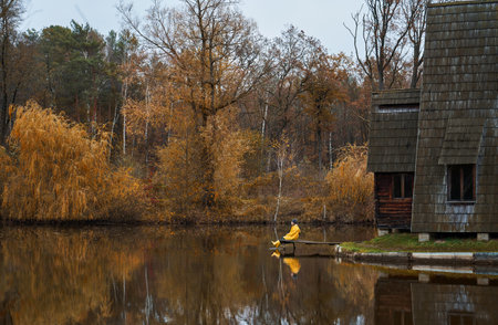 Panoramic image autumn landscape, girl in yellow clothes sitting on pier, calm water surface of the lake reflects orange foliage and treesの写真素材