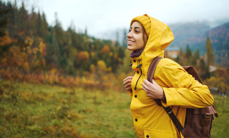 Portrait happy hiker girl in yellow wear and backpack traveling in mountains alone, into the wild...