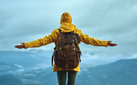 Rear view woman in mountains, wearing yellow warm clothes with backpack. standing with open hands, enjoying frosty nature sceneryの写真素材