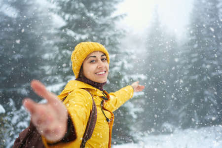 Happy joyful woman in yellow warm clothing at winter forest with falling snow. Outdoor Christmas vacationの写真素材