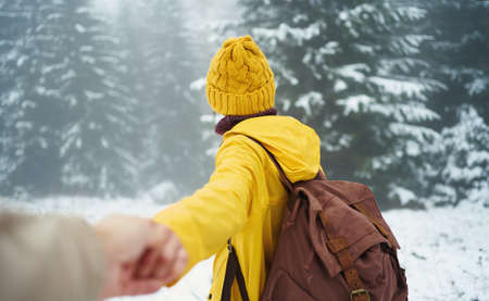 Follow me, first person view of girl with backpack going to snowy mysterious forest, couple at winter Christmas vacation outdoorsの写真素材