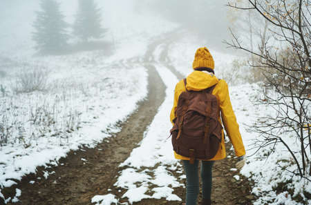 Hiking woman with backpack walking by trail in winter foggy forest covered snow. Adventure people in wild natureの写真素材