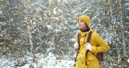 Travel woman hiking in the wild frosty forest covered snow. Wearing. yellow winter clothes and backpack. Winter is coming, first snowfallの写真素材