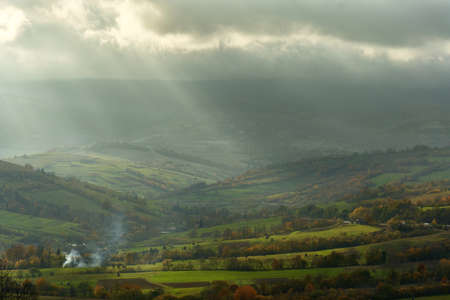 Panoramic image of hills in the fog, misty foggy landscape with sun rays shine through the cloudy skyの写真素材