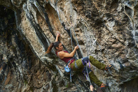 Side view strong muscular woman rock climber gripping hold, working on challenging route on cliffの写真素材