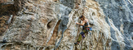 Panoramic image of powerful athletic woman climbing on beautiful rock wall, strong human body on stone cliff textureの写真素材
