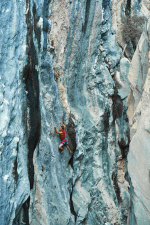 Beautiful blue bright crag wall, texture dramatic and colorful erosional water formation. Sporty man climbing up on hard routeの写真素材