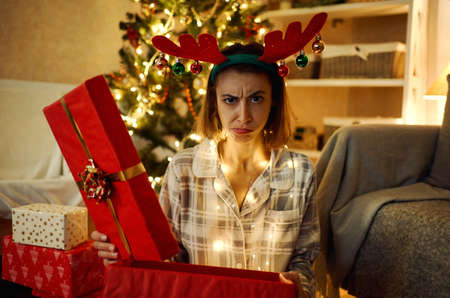 Portrait of displeased upset female frowns face as disappointed, hold dislike gift on Christmasの写真素材