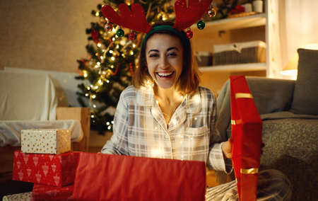 Portrait laughing looking happy woman opening Christmas gift box at home, giving presents conceptの写真素材
