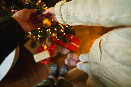 Couple holds in hands xmas toy golden ball to decorate xmas tree. Winter holiday, preparing to celebrate Christmas and New Year at homeの写真素材