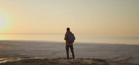 Silhouette man traveler standing in front salt lake coast, meeting golden sunrise, enjoying calm and nature beautyの写真素材