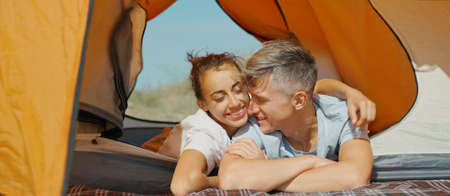 Tourists couple relaxing together in orange tent during vacation or weekend. Relationship, camping lifeの写真素材