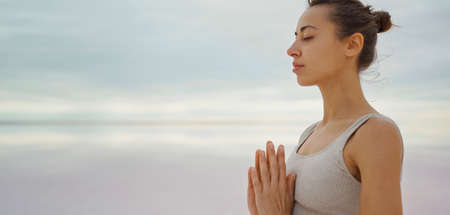 Close-up portrait becalmed woman practicing yoga and meditation outdoors with sky and lake view, namaste gesture. Harmony with nature and peace of mindの写真素材