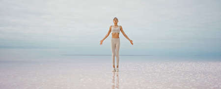 Beautiful calmness landscape, young woman practicing yoga meditation, standing at deserted endless salt pink lake beachの写真素材