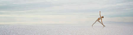 Panoramic view of peaceful landscape, sporty woman doing yoga exercise at deserted endless salt lake beachの写真素材