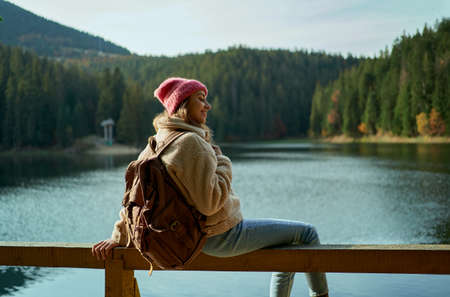 Inspired joyful woman hiker sits on wooden pier at beautiful mountain lake with turquoise water and enjoys her trip into the wild nature locationの写真素材