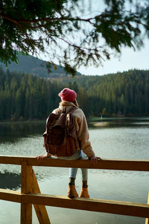 Rear view hiker woman sits on wooden pier by beautiful mountain lake and enjoys amazing calm forest landscape. Wild nature beauty, healthy active lifestyle.の写真素材