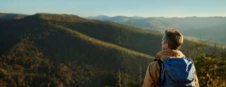 Panoramic nature view of mountains and hills with woods at sunset, back view man hiker admiring landscape, travel point destinationの写真素材