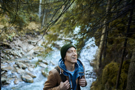 Outdoors portrait positive man hiker with backpack by the river at the forest, enjoying fresh air,...