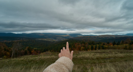 First person view of hand shows to beautiful landscape with hills, mountains and meadow with...