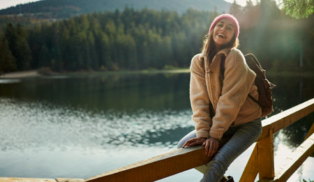 Pleased laughing woman sits on pier near mountain lake. Tourist woman enjoying the day outdoors in nature landscapeの写真素材