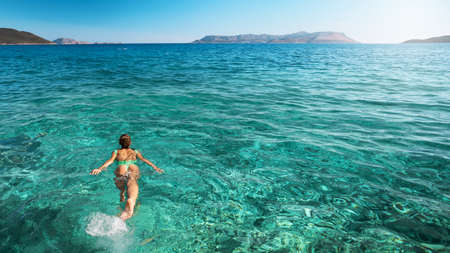 Panoramic view of summer girl in green swimsuit bikini swimming in clear turquoise sea water. Vacation at Paradise. Ocean relax, travel to islandの写真素材