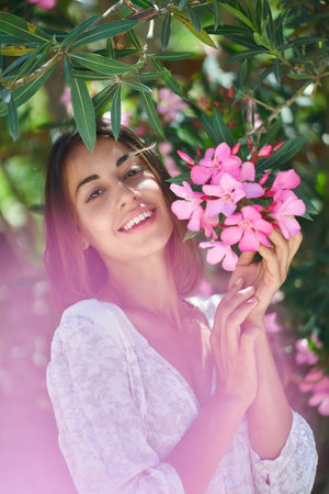 Elegant pretty pleased woman enjoying flowers aoma in spring garden with pink glowの写真素材