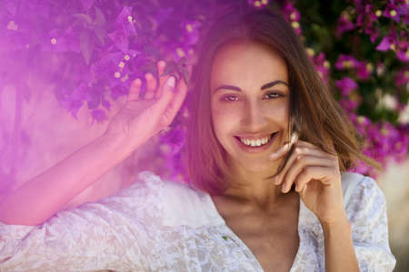 Close up beauty portrait woman with charming smile and smooth skin in spring garden with pink flowersの写真素材