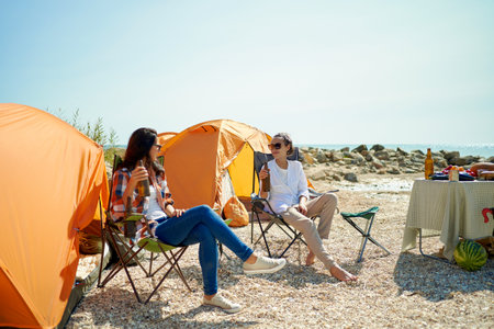Two women friends drinking cold beer at hot day in camping, joyful girls having fun together during weekendの写真素材