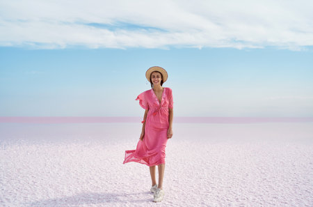 Panoramic beautiful landscape of salt flats on pink lake with blue cloudy sky, looks like white desert. Elegant girl in flowing pink dress enjoying walkの写真素材