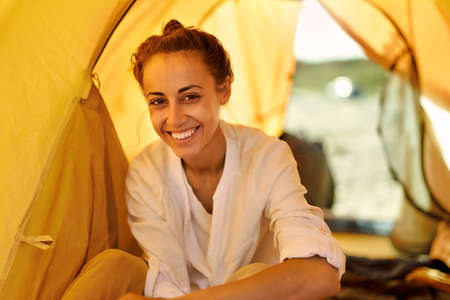 Headshot portrait of smiling authentic emotions woman inside tent during vacation or weekend, enjoying camping lifeの写真素材