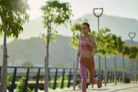 Fitness woman sprinting on bridge road at tropical park. Healthy young runner jogging exercising at morningの写真素材