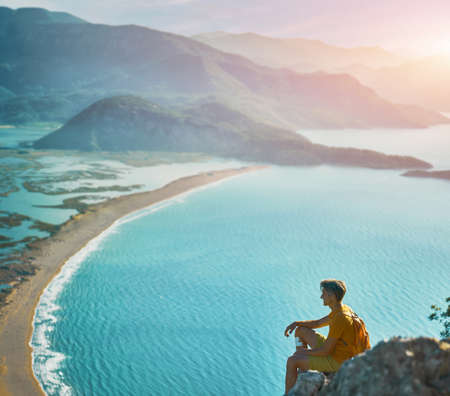 One tourist man adventure travel explorer hiker sits on mountain cliff, looking at panoramic landscape sea view. Go everywhere conceptの写真素材
