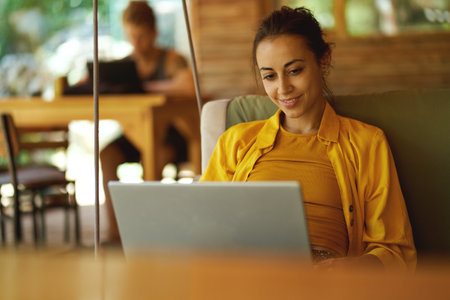 Young charming brunette woman in cafe at summer day with her portable laptop, business startup freelancer or designer works on laptop in coworking hubの写真素材